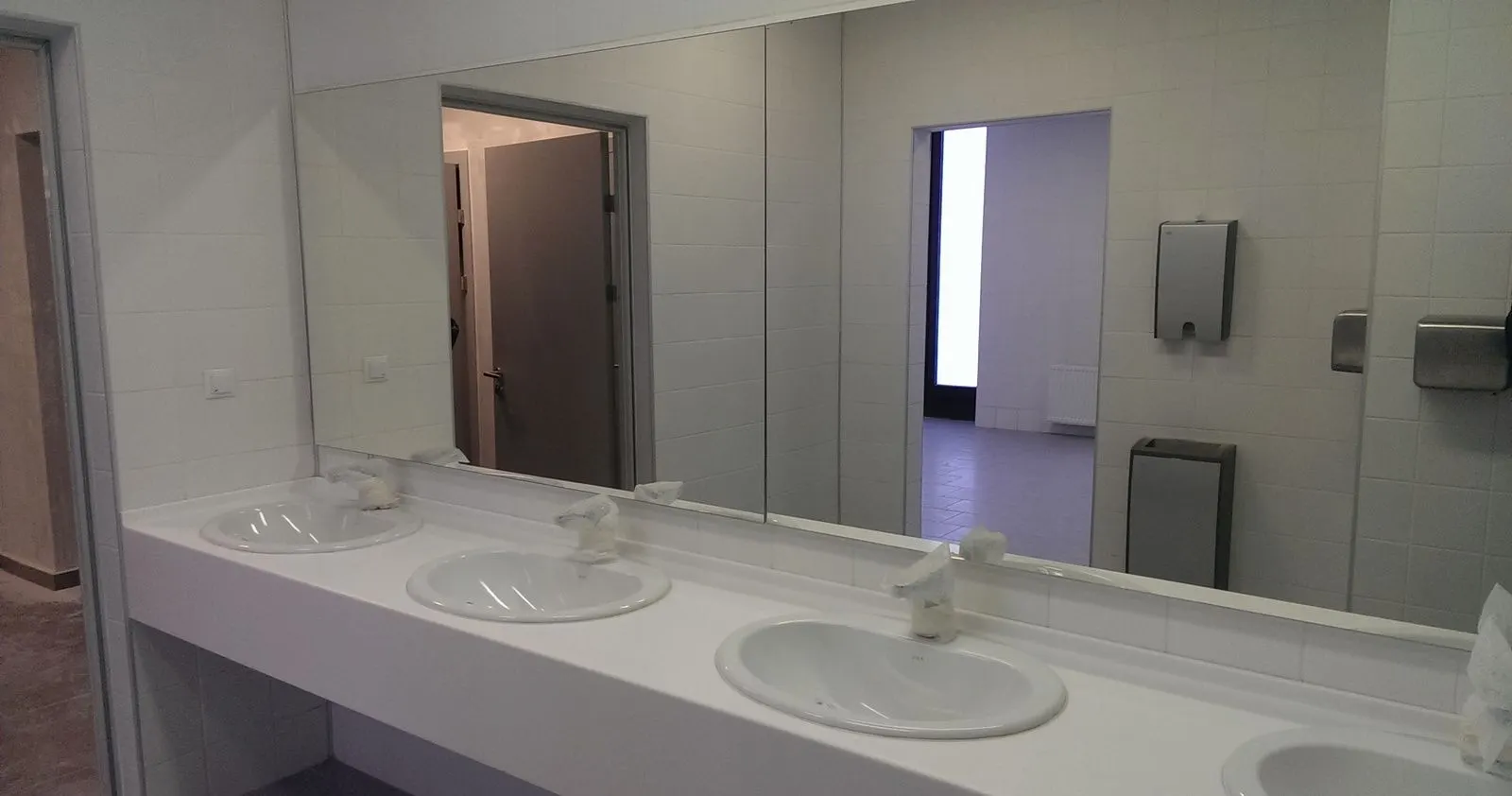 Airport washroom with a long white solid surface vanity and inset basins