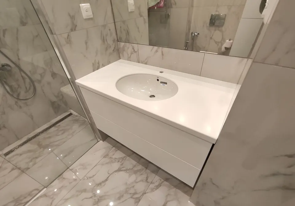 White solid surface vanity top with integrated basin next to a walk-in shower