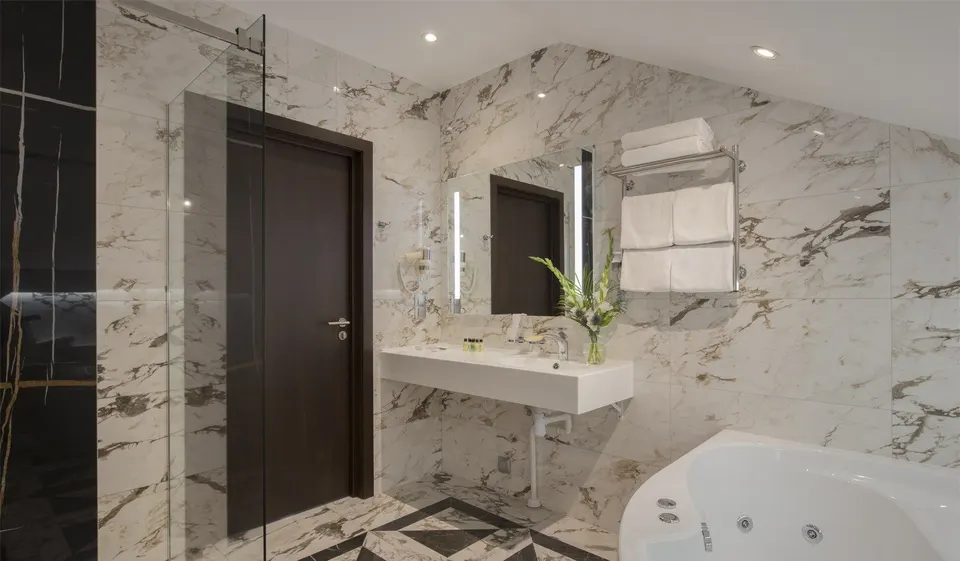Hotel bathroom with marble-effect tiles, corner bath and a wall-hung white solid surface vanity