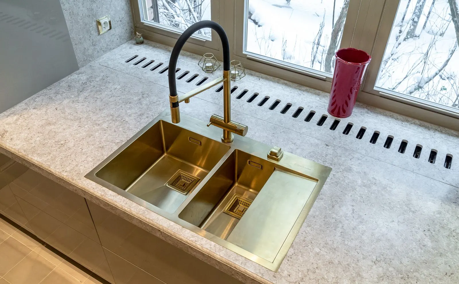 Veined solid surface worktop with a brass undermount sink under a window