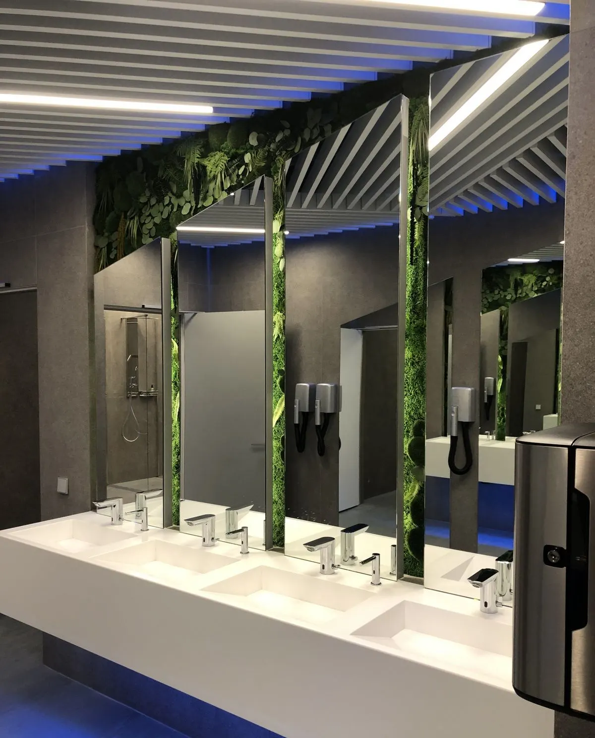 Public washroom with a long white solid surface multi-station washbasin and backlit plinth