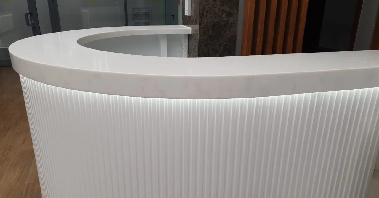 Curved reception desk with a veined solid surface top and backlit fluted front