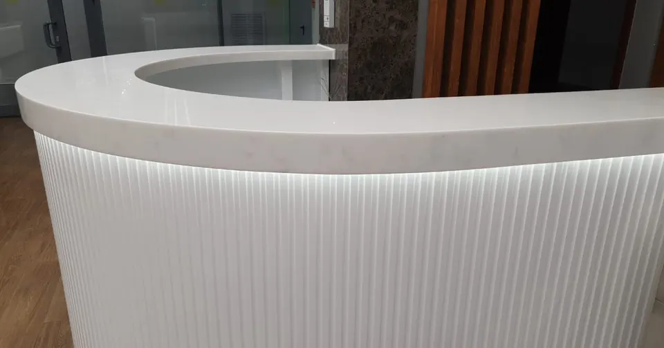 Curved reception desk with a veined solid surface top and backlit fluted front