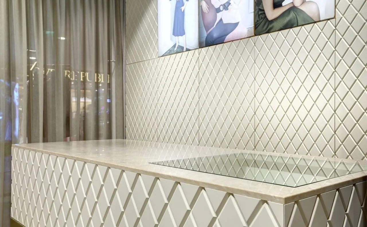 Shop counter with a veined solid surface top in front of a 3D diamond-pattern wall