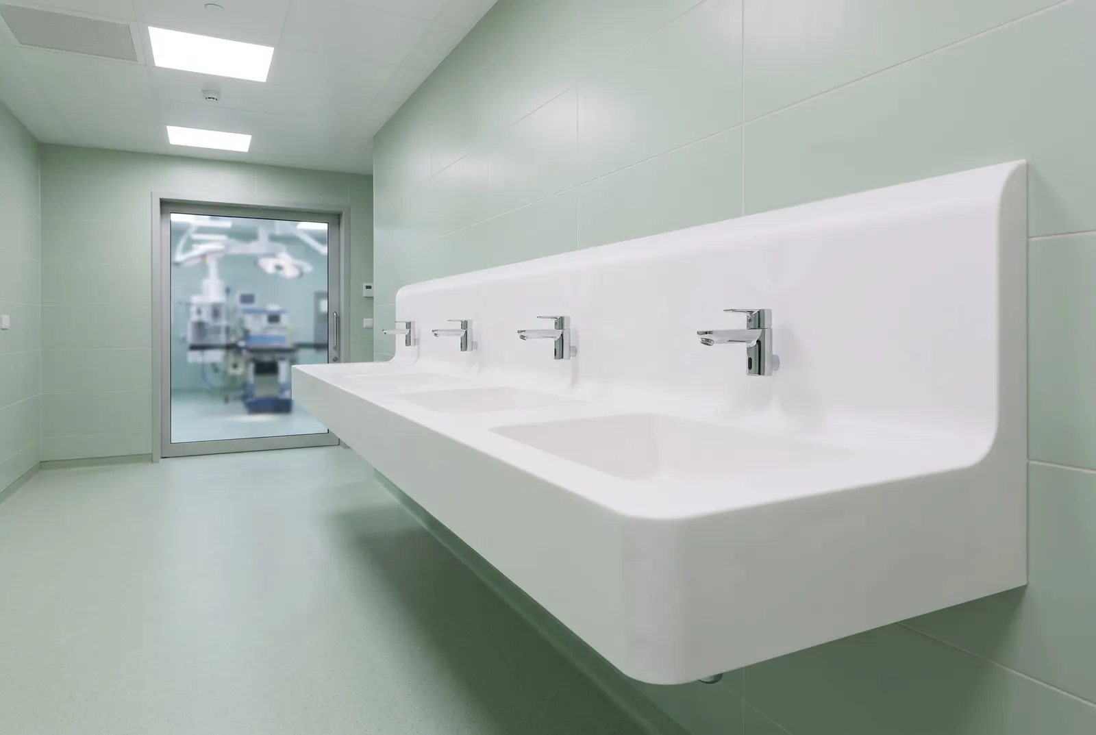 3D visualisation: wall-hung multi-station surgical scrub basin in white solid surface outside an operating theatre