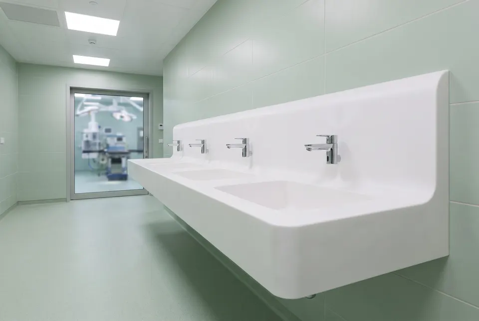 3D visualisation: wall-hung multi-station surgical scrub basin in white solid surface outside an operating theatre